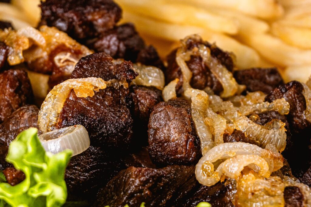 Photo en gros plan de bœuf grillé surmonté d'oignons, accompagné de frites et de laitue.