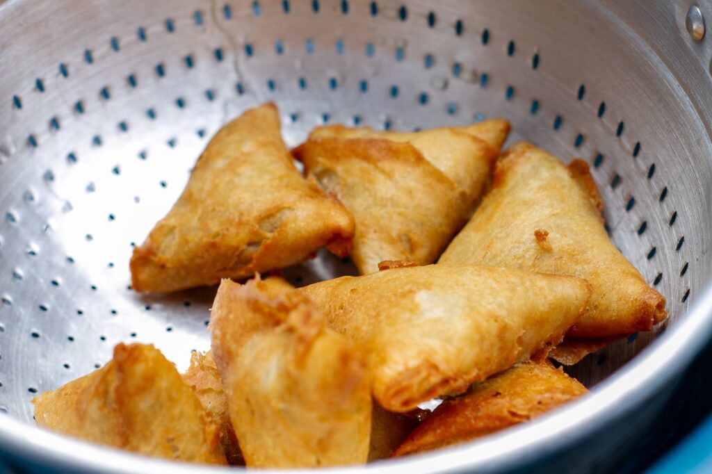 Des samosas frits croustillants et dorés placés dans une passoire en acier inoxydable, parfaits pour un en-cas salé.