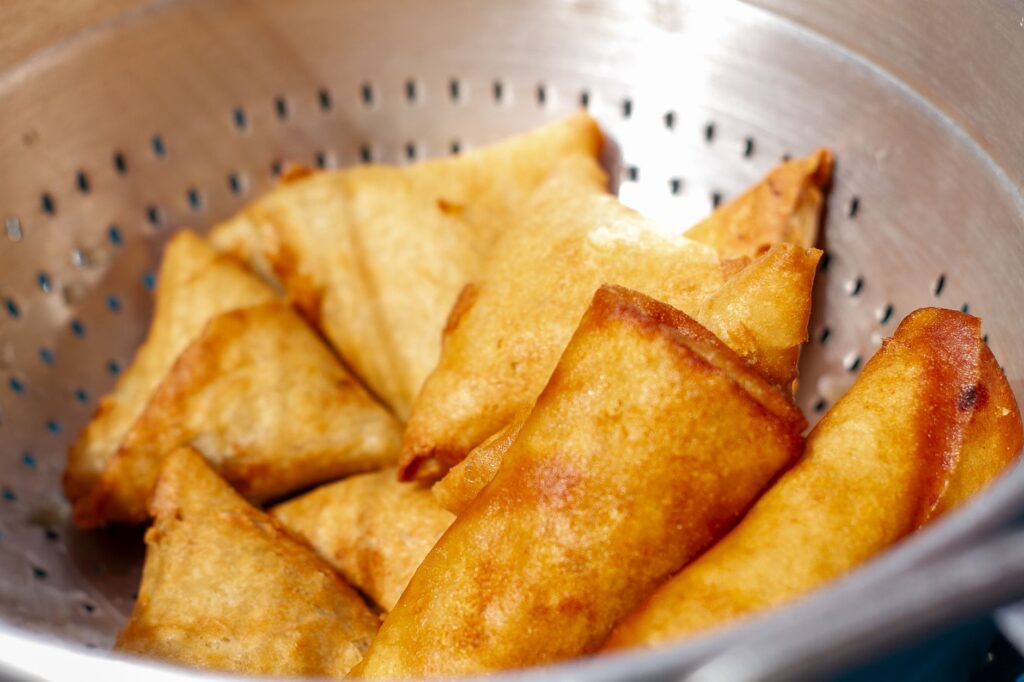 Gros plan sur des samosas frits dorés refroidissant dans une passoire en métal, parfaits pour une collation.