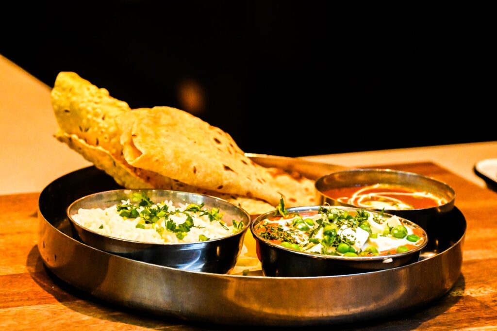 Thali indien exquis avec pain naan, curry de paneer et riz aromatique servi sur une table en bois.