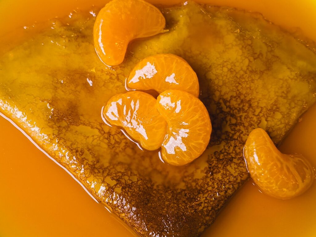 Gros plan d'une délicieuse crêpe garnie de tranches de mandarine juteuses dans un sirop sucré.