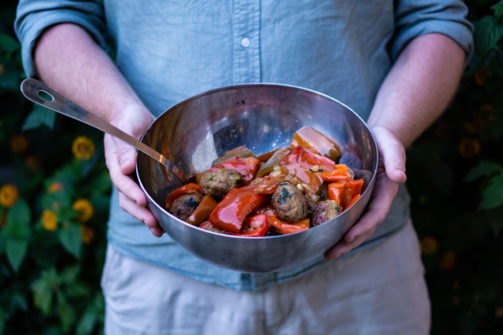 Délicieuse ratatouille maison et boulettes de viande servies dans un grand bol, tenues en extérieur contre un décor naturel.