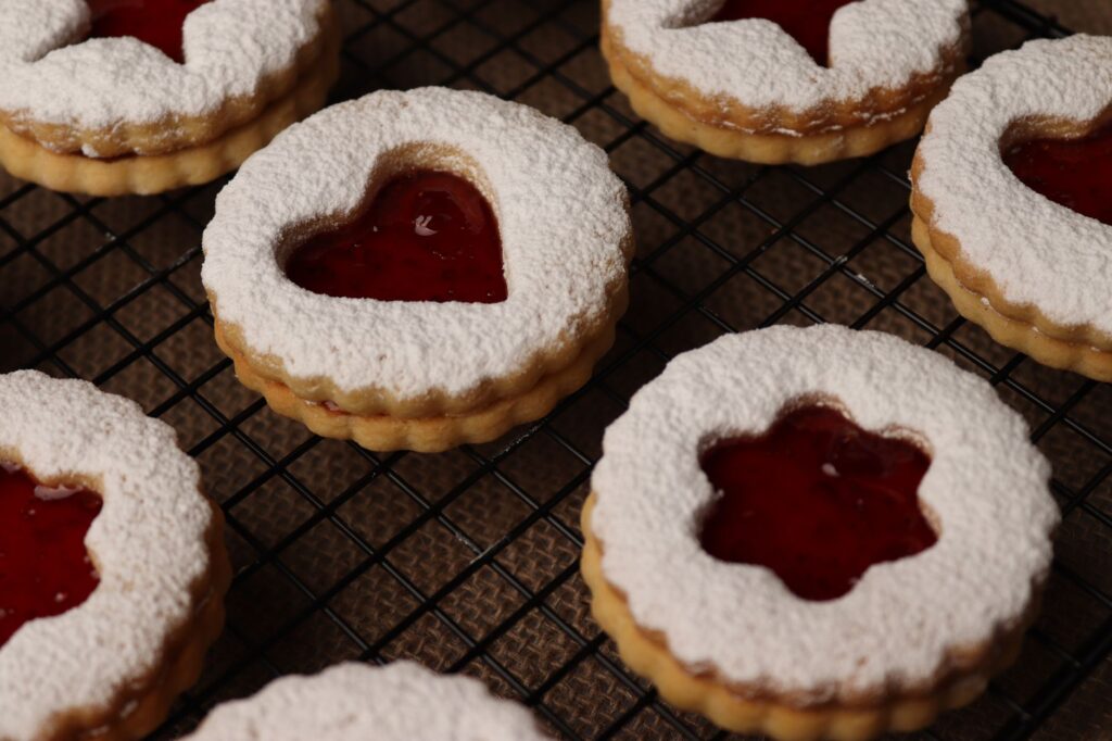 Cookies Linzer en forme de cœur avec confiture de framboise, parfaits pour les fêtes ou les occasions spéciales.