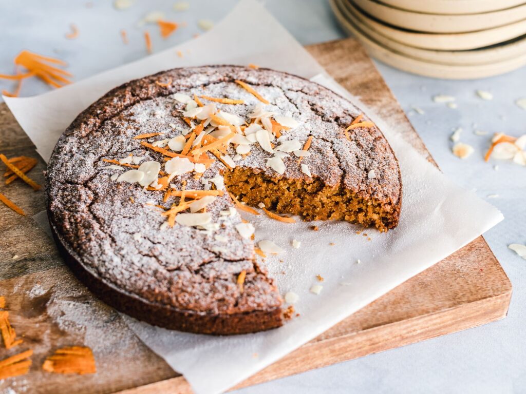 Un gâteau aux carottes rustique avec des amandes sur une planche en bois, parfait pour le dessert.