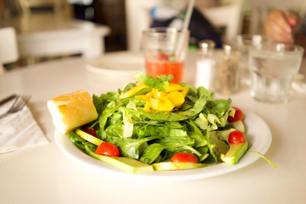 Salade verte saine avec tomates cerises, laitue et mangue sur une assiette blanche avec du pain.