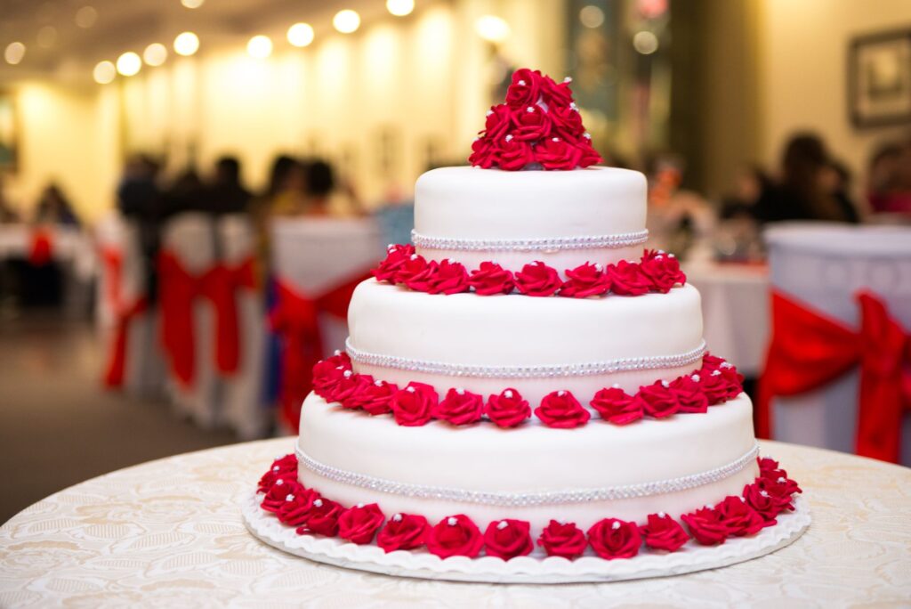 Un magnifique gâteau de mariage à trois niveaux orné de roses rouges vibrantes lors d'une réception formelle.