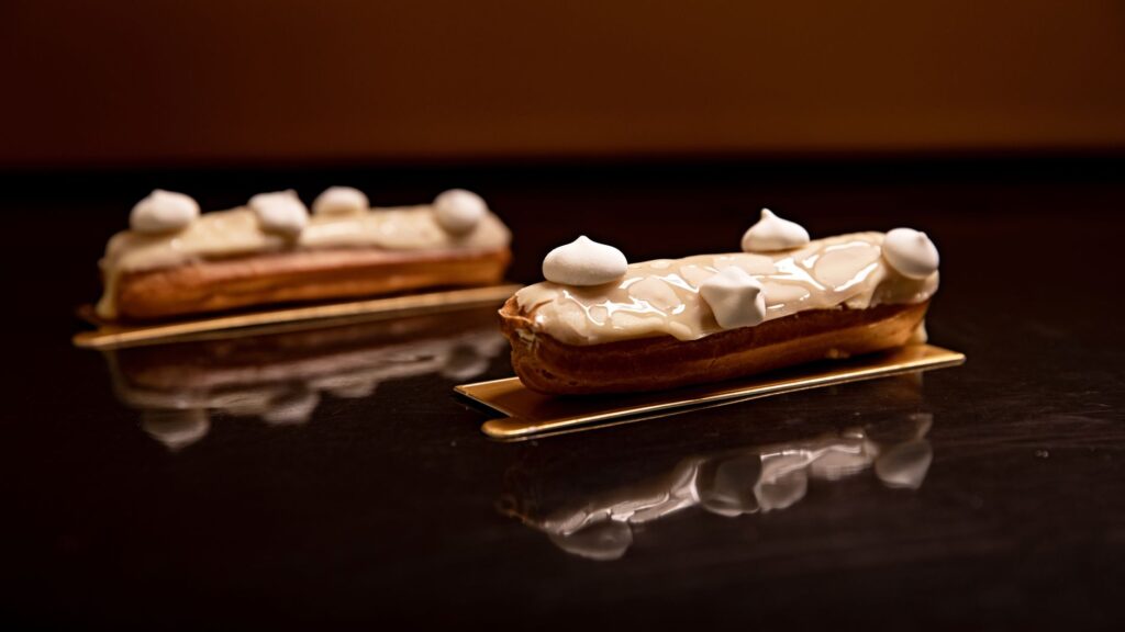 Gros plan de deux éclairs garnis de crème brillante sur une surface réfléchissante.
