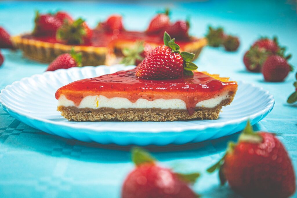 Une part alléchante de cheesecake aux fraises garnie de fraises fraîches sur une assiette bleue.