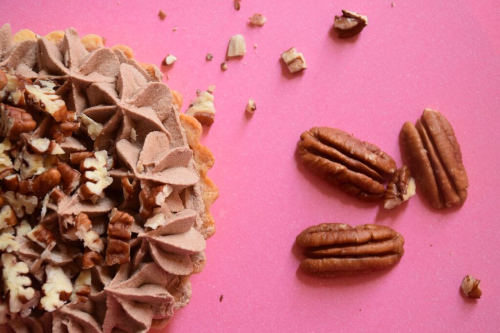 Gros plan sur une tarte au chocolat et aux pacanes avec des noix sur un arrière-plan rose.