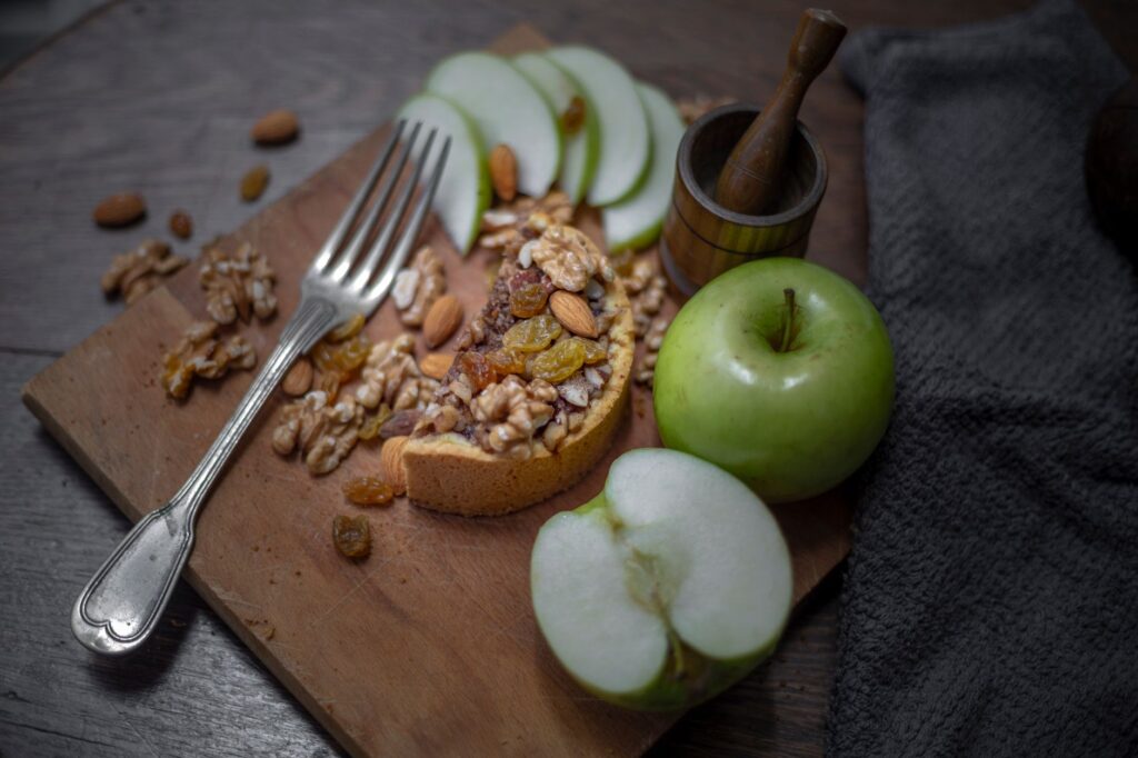 Une délicieuse tarte rustique aux noix, raisins secs et pommes vertes fraîches sur une planche en bois.