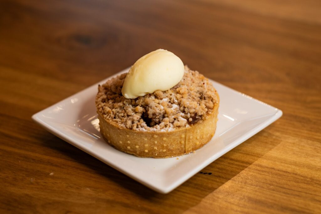 Tarte crumble aux pommes savoureuse garnie de glace à la vanille sur une assiette blanche, parfaite pour le dessert.