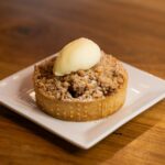 Tarte crumble aux pommes savoureuse garnie de glace à la vanille sur une assiette blanche, parfaite pour le dessert.