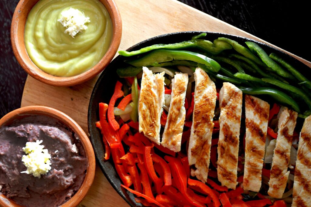Fajitas de poulet grillé grésillant avec poivrons, guacamole et haricots frits sur une planche de bois.