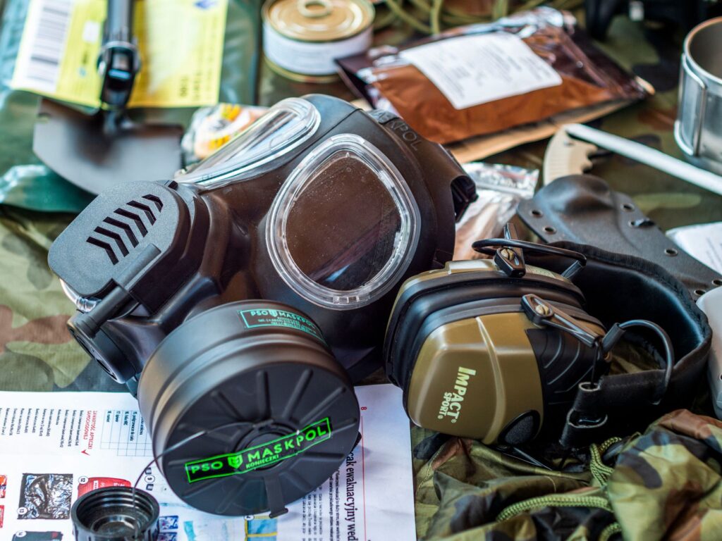 Équipement de survie comprenant un masque à gaz et un casque tactique sur fond camouflage.