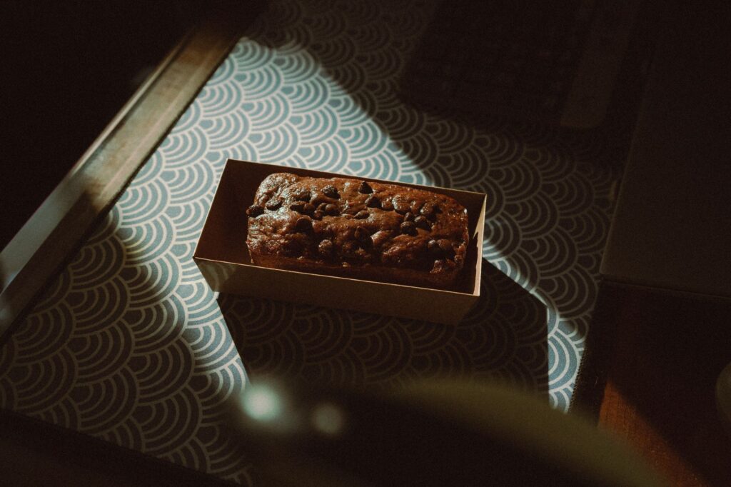 Un délicieux gâteau au chocolat garni de pépites de chocolat dans une boîte, capturé dans un éclairage intérieur chaleureux.