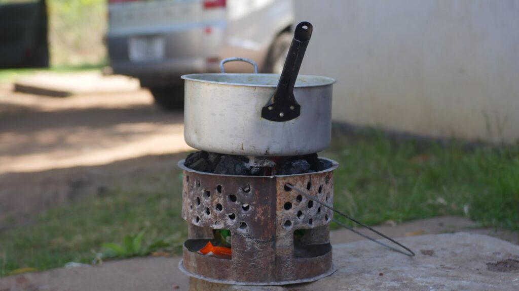 Une casserole en métal est posée sur un poêle à charbon rustique en extérieur, créant une scène de cuisine traditionnelle.