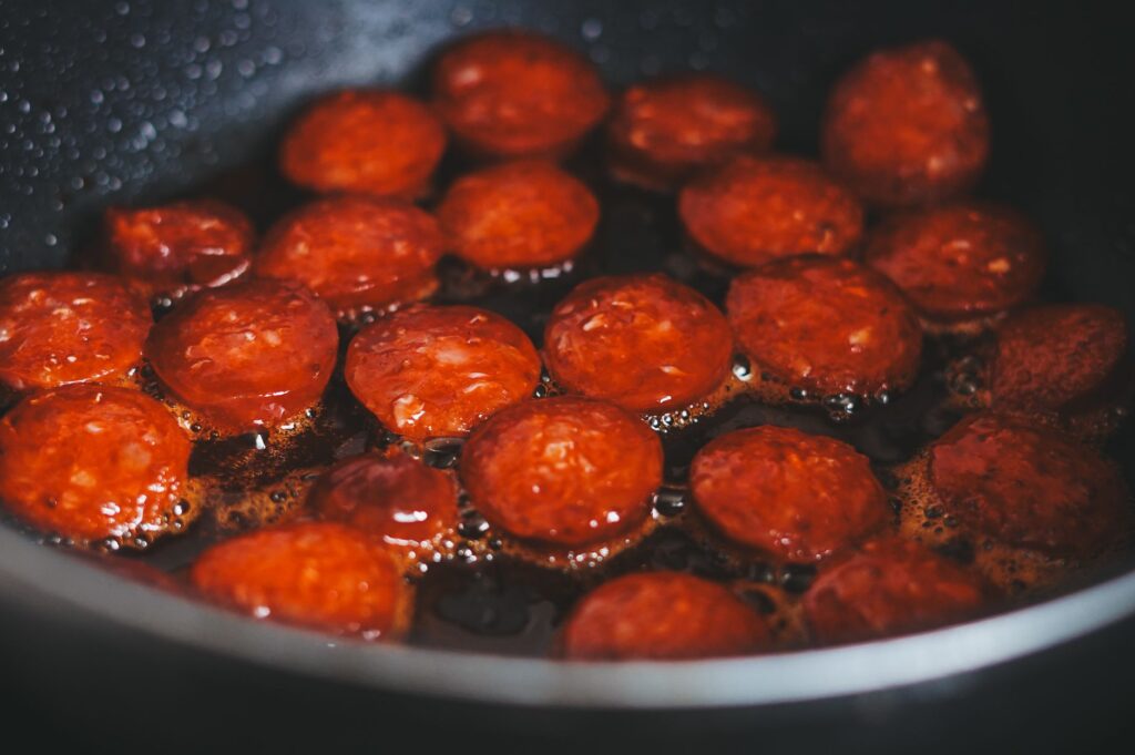 Gros plan de saucisses tranchées en train de frire dans une poêle, mettant en valeur leur texture riche et croustillante et leur couleur vibrante.