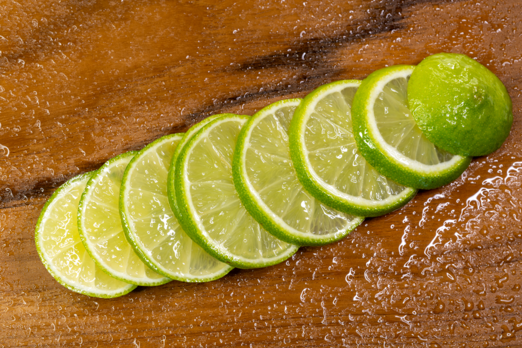 Tranches de citron vert rafraîchissantes posées sur une surface en bois humide, idéales pour les thèmes culinaires et estivaux.