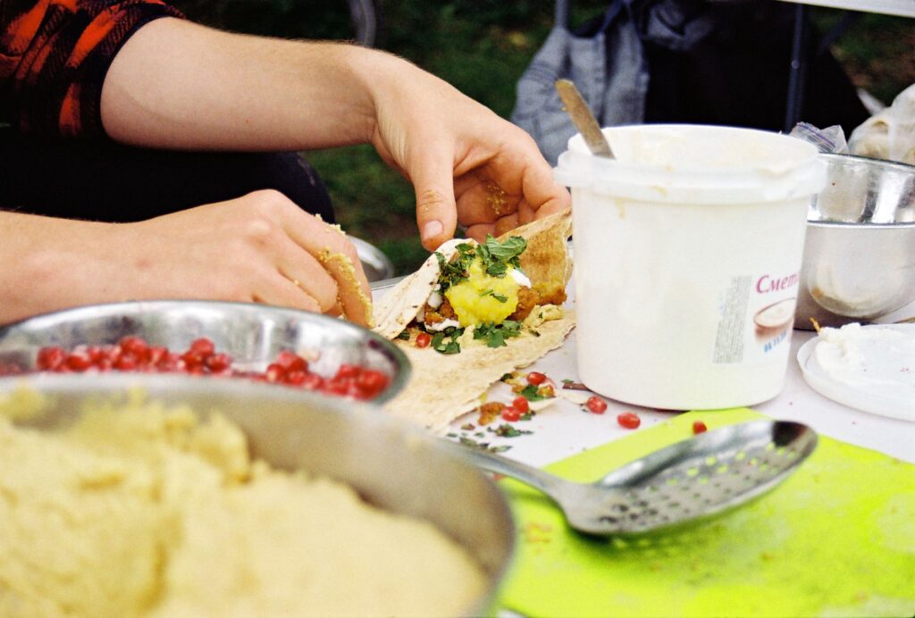Gros plan de mains préparant un wrap de falafel frais avec des herbes et des graines de grenade, mettant en valeur des ingrédients sains.