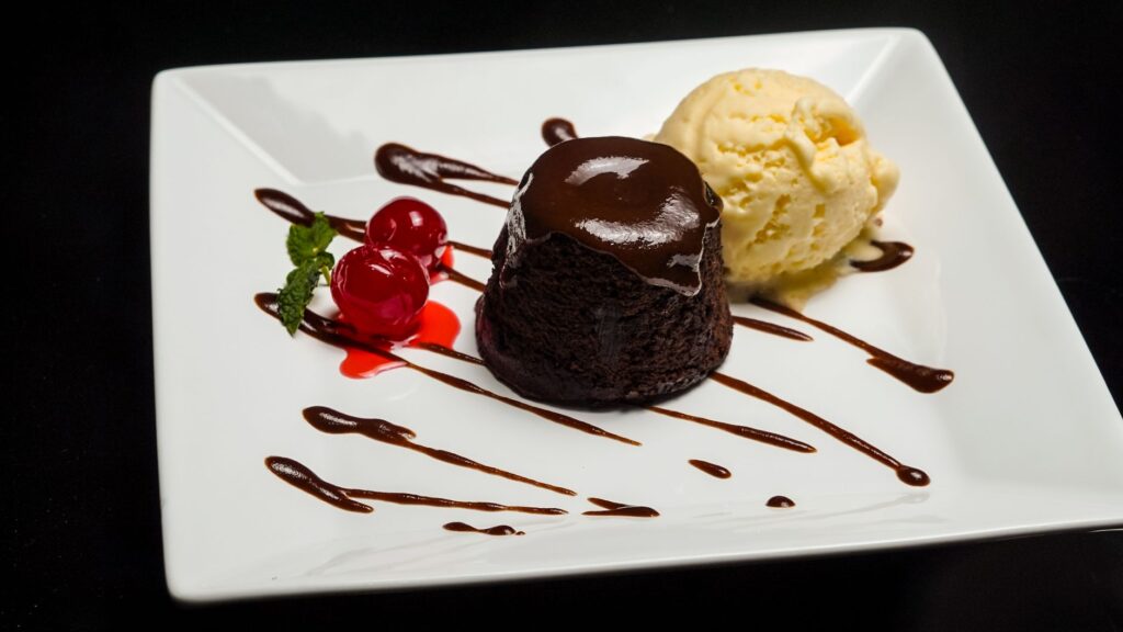 Délicieux gâteau au chocolat coulant servi avec de la glace à la vanille et des cerises sur une assiette blanche.