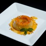 Un flan au caramel joliment présenté avec des feuilles de menthe et des noix, sur un fond noir.