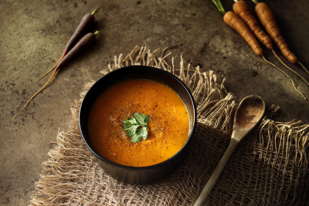 Soupe de carottes tiède dans un bol noir, garnie de persil sur un tapis texturé.