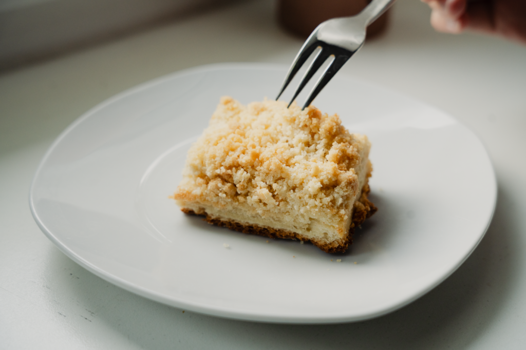 Gros plan sur une tranche de Streuselkuchen avec une fourchette sur une assiette blanche.