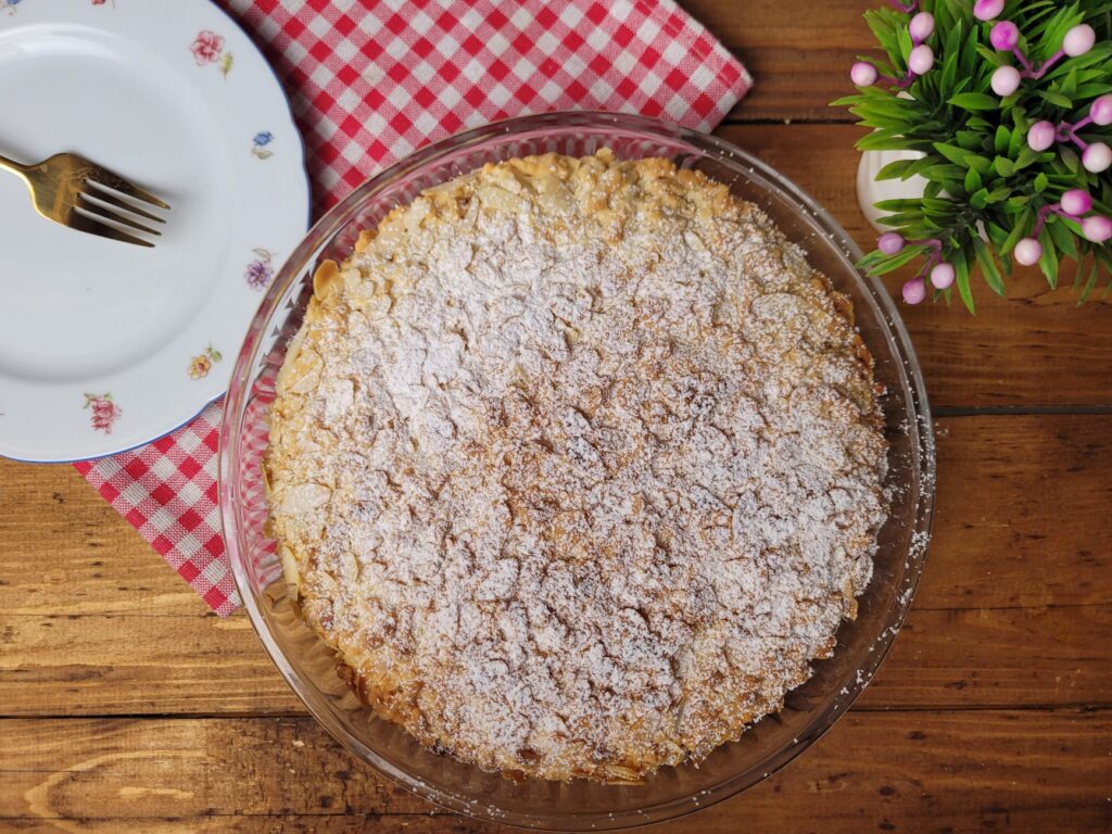 Vue de dessus d'une tarte aux pommes fraîchement cuite, saupoudrée de sucre en poudre, posée sur une table en bois.