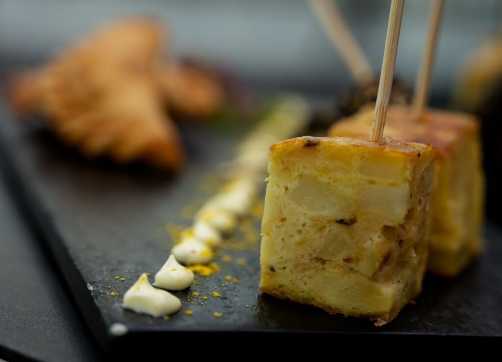 Gros plan sur une tortilla argentine traditionnelle servie avec de l'aïoli sur une assiette en ardoise noire, illustrant la présentation culinaire.