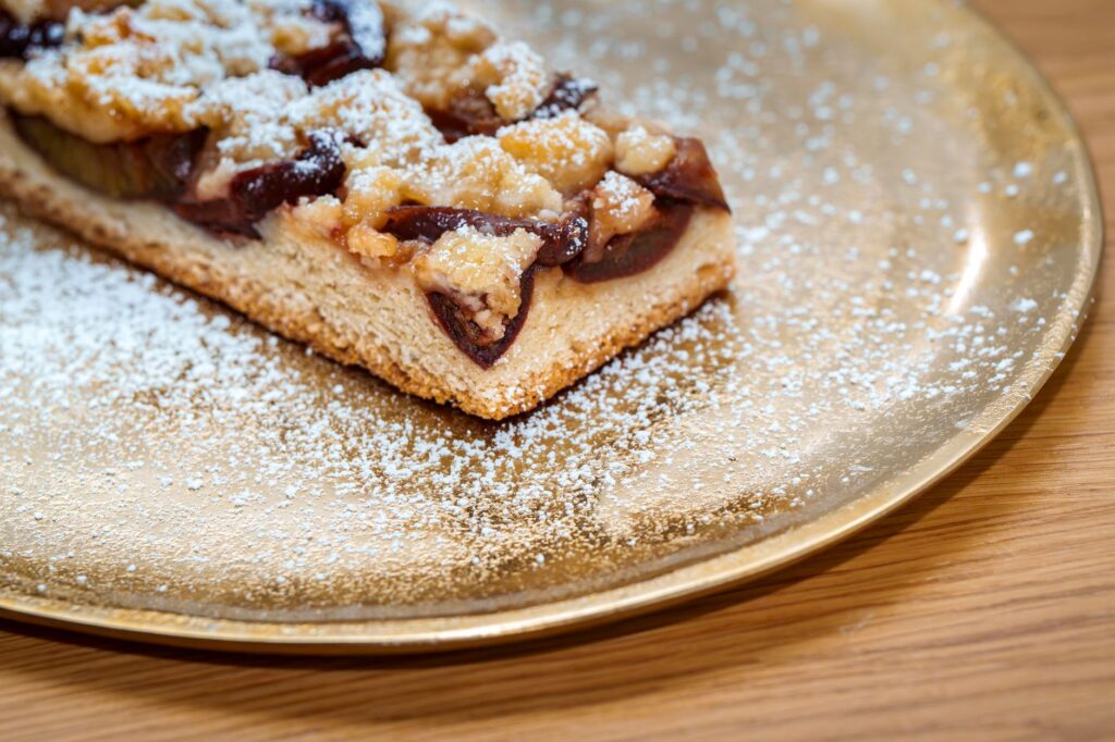 Un gros plan d'une délicieuse tarte aux prunes saupoudrée de sucre glace, servie sur une assiette dorée.