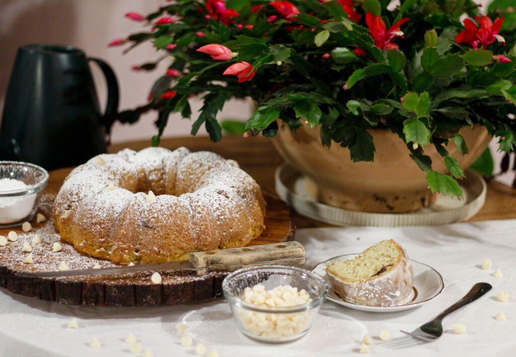 Un délicieux gâteau Bundt saupoudré de sucre, accompagné de fleurs éclatantes et de pépites de chocolat blanc.