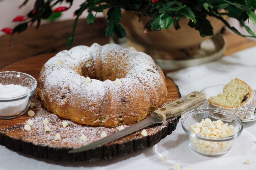 Délicieux gâteau Bundt saupoudré de sucre glace et de chocolat blanc, présenté sur une planche en bois, parfait pour une pause gourmande.