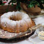 Délicieux gâteau Bundt saupoudré de sucre glace et de chocolat blanc, présenté sur une planche en bois, parfait pour une pause gourmande.