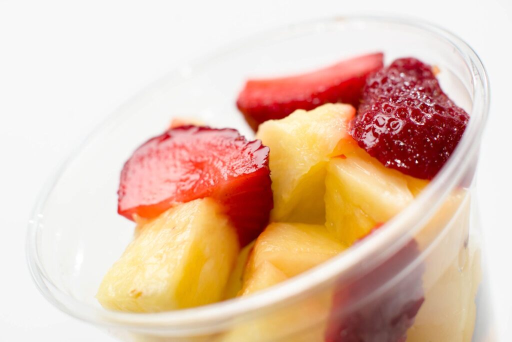 Gros plan sur une salade de fruits frais dans une tasse transparente avec des fraises et de l'ananas tranchés.
