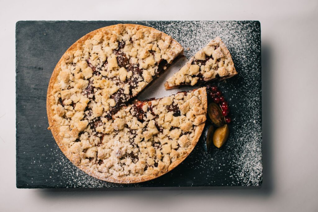Vue de dessus d'une tarte crumble aux fruits rouges sur une ardoise foncée, saupoudrée de sucre glace.