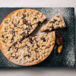 Vue de dessus d'une tarte crumble aux fruits rouges sur une ardoise foncée, saupoudrée de sucre glace.