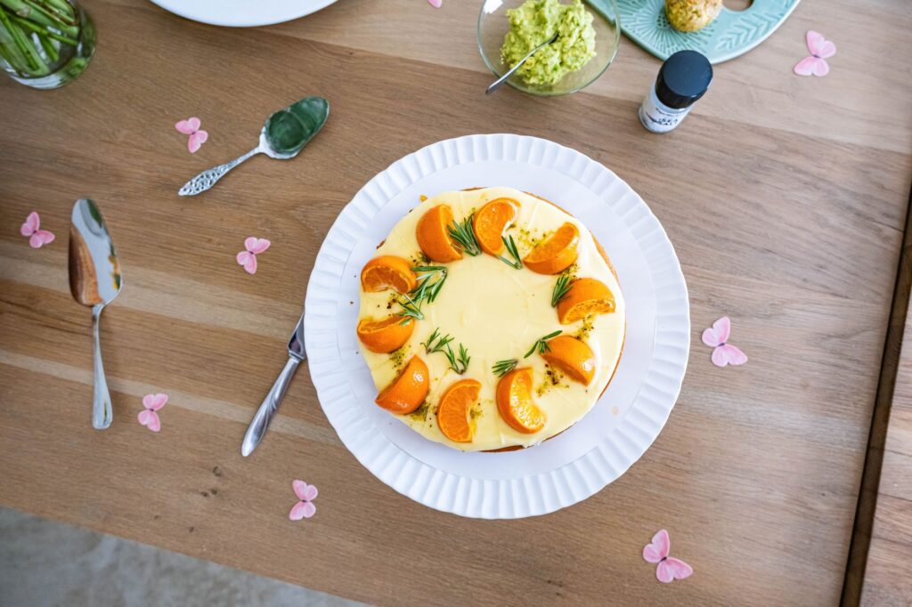 Vue de dessus d'un cheesecake magnifiquement décoré d'oranges et de romarin, présenté sur une table en bois.