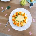 Vue de dessus d'un cheesecake magnifiquement décoré d'oranges et de romarin, présenté sur une table en bois.