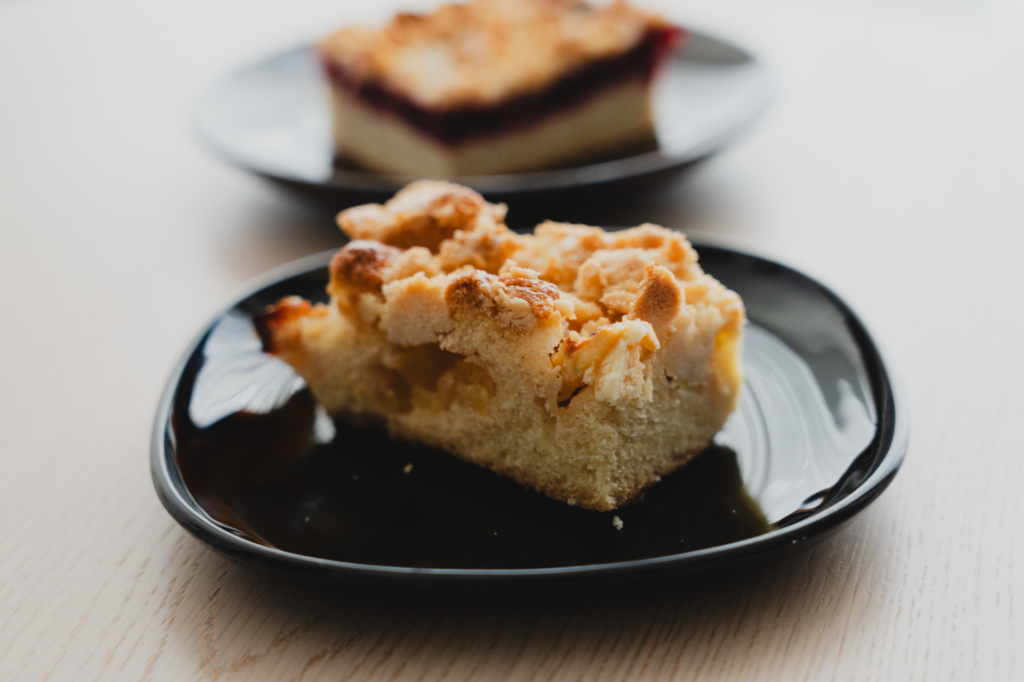 Gros plan sur une tranche de gâteau streusel aux pommes présentée sur une assiette noire, mettant en valeur son crumble.