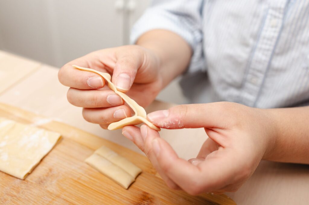 Dans une cuisine chaleureuse, des mains façonnent habilement de la pâte à pâtes fraîches sur une planche en bois.