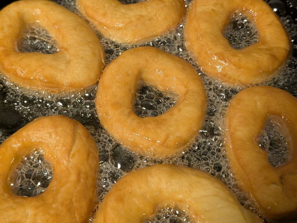 Des beignets dorés frits dans l'huile chaude, révélant en gros plan leur texture croustillante et leurs bulles.
