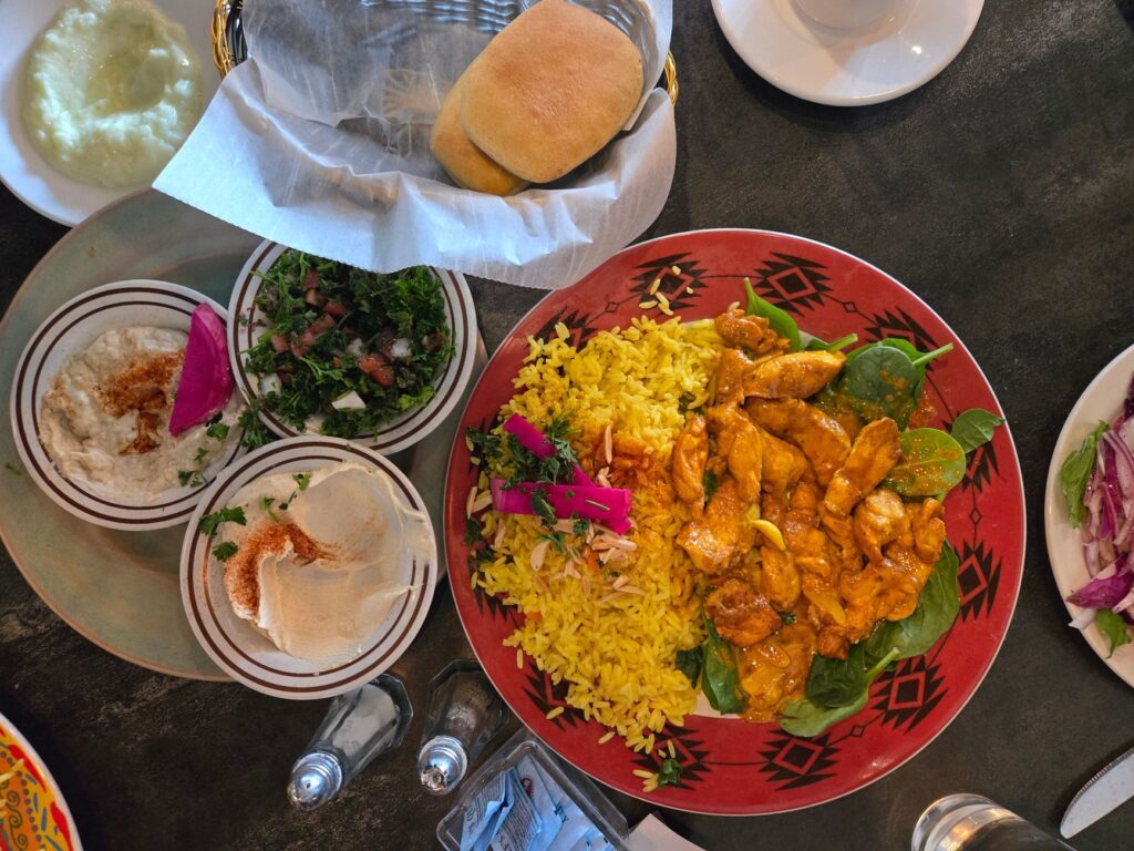 Un repas vibrant du Moyen-Orient avec du curry de poulet, du riz, du houmous, de la salade et du pain.