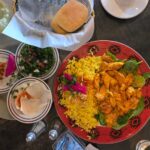 Un repas vibrant du Moyen-Orient avec du curry de poulet, du riz, du houmous, de la salade et du pain.