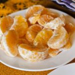 Gros plan sur des tranches de mandarine juteuses disposées sur une assiette blanche, capturant un aspect frais et éclatant.