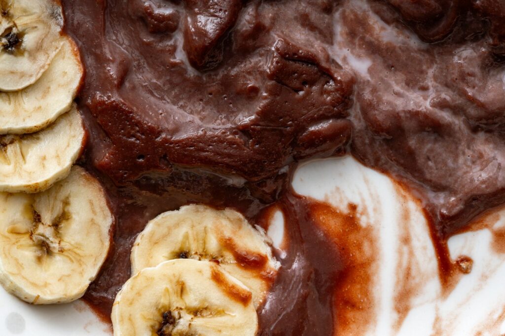 Gros plan sur des tranches de banane nappées d'une riche pâte à tartiner au chocolat sur une assiette blanche, mettant en valeur les textures et le contraste.