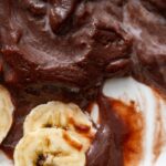 Gros plan sur des tranches de banane nappées d'une riche pâte à tartiner au chocolat sur une assiette blanche, mettant en valeur les textures et le contraste.