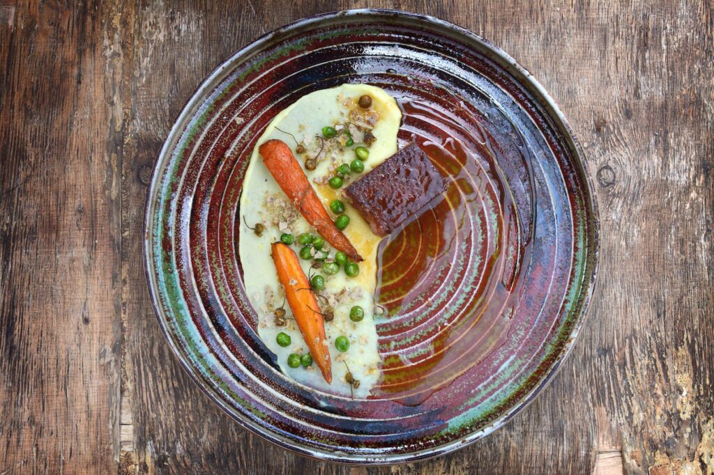Présentation d'un plat gastronomique avec des carottes et des pois sur une assiette rustique. Idéal pour les besoins de photographie culinaire.
