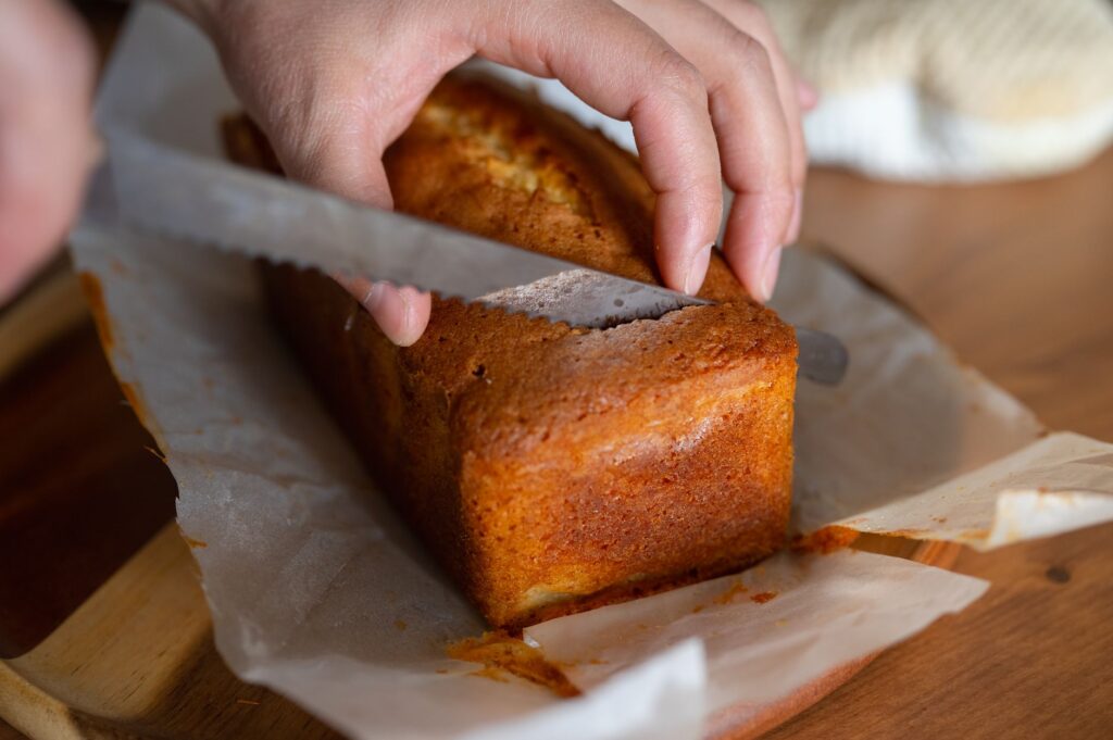 Gros plan sur des mains découpant un gâteau fraîchement cuit sur du papier sulfurisé.