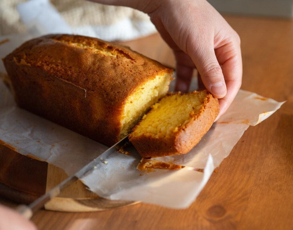 Gros plan sur une main coupant un quatre-quarts fait maison, révélant la croûte dorée et la texture moelleuse.