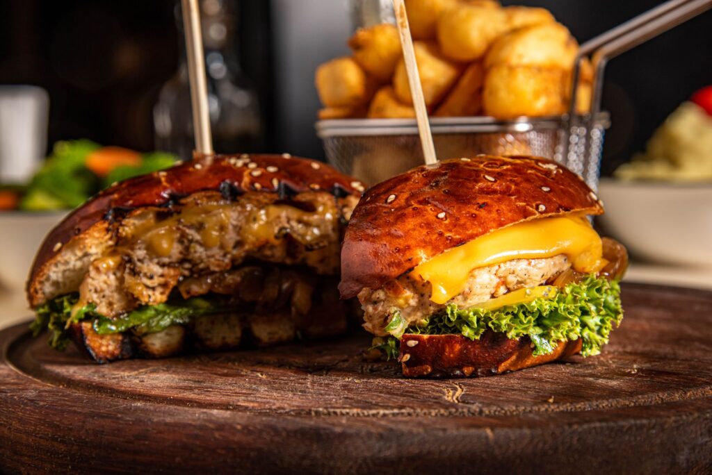 Gros plan sur un hamburger juteux au cheddar, laitue et tater tots sur un plateau en bois.